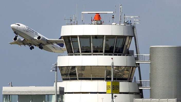 Ein Flugzeug in der Luft, im Vordergrund sieht man den Tower