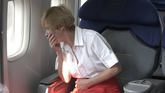 Eine Frau sitzt im Flugzeug, schaut aus dem Fenster und hält sich die Hand vor den Mund