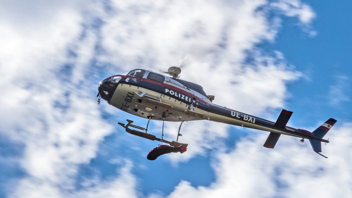 Weißblauroter Polizeihubschrauber fliegt vor einem blauen Himmel mit weißen Wolken.