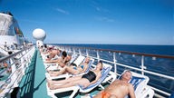 Viele Menschen liegen aufgereiht auf Sonnenliegen auf einem Kreuzfahrtschiff