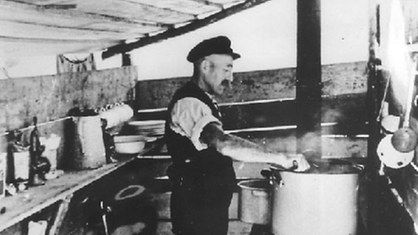 Historische Schwarzweißaufnahme: Ein Koch in seiner Küche auf einem der Holländerflöße