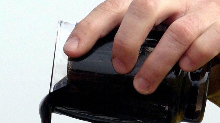 Großaufnahme einer Hand, die eine schwarze Flüssigkeit aus einem Glas ausgießt