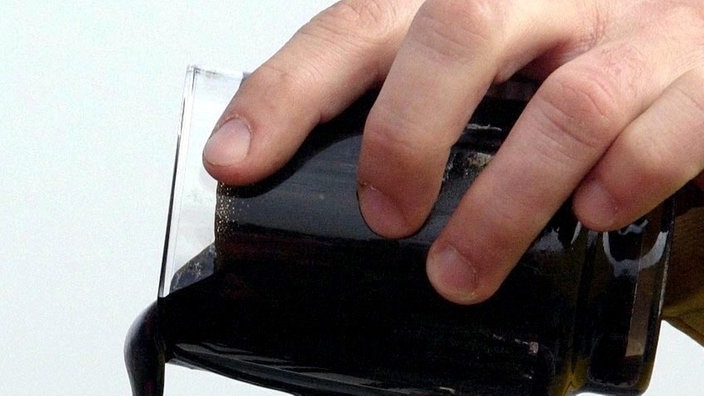 Großaufnahme einer Hand, die eine schwarze Flüssigkeit aus einem Glas ausgießt | Bildquelle: ddp/dadp/Jens Köhler Großaufnahme einer Hand, die eine schwarze Flüssigkeit aus einem Glas ausgießt
