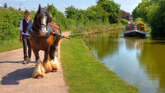 Ein Pferd zieht auf einem Treidelpfad ein kleines Schiff den Kanal hoch