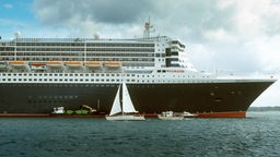Die Queen Mary 2 vor Anker. Eine Segeljacht passiert das Kreuzfahrtschiff