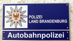 Rechteckiges Blechschild: Auf blauem Grund ist in weißer Schrift Polizei Brandenburg, Autobahnpolizei zu lesen. Links oben ist das Länderwappen von Brandenburg zu sehen