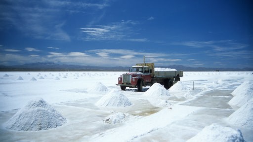 Mehrere weiße Haufen mit Lithium umgeben von Flüssigkeit, im Hintergrund fährt ein Transport-LKW