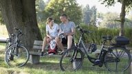 Ein Mann und eine Frau sitzen im Grünen auf einer Bank, neben ihnen stehen E-Bikes 