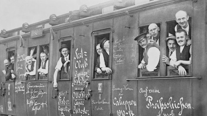 Soldaten schauen aus einem Waggon, auf dem unter anderem der Schriftzug 'auf zum Preisschießen nach Paris' steht