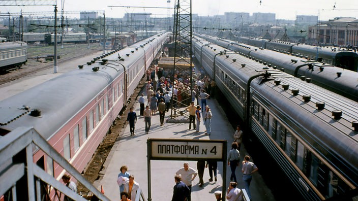Ein Bahnsteig mit vielenMenschen. Links und rechts stehen Züge auf den Gleisen