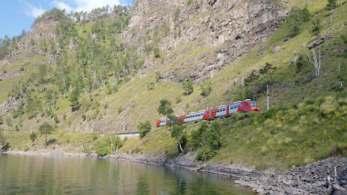 Ein Personenzug fährt an einem See entlang
