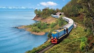 Ein Zug der Transibirischen Eisenbahn fährt an einem Seeufer entlang