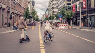 Ein Mann mit einem E-Roller und eine Frau auf einem Fahrrad fahren in der Friedrichstraße in Berlin.