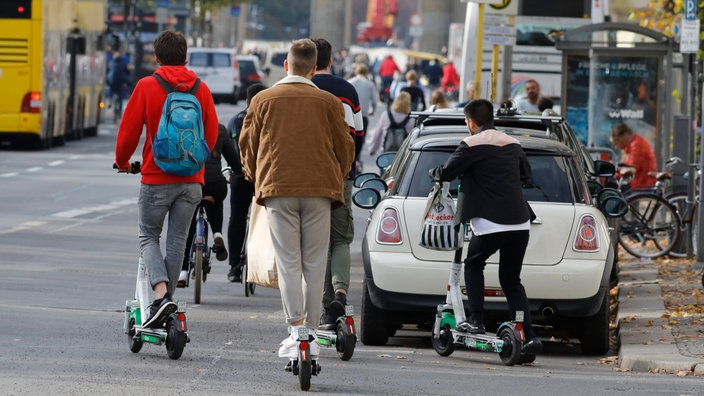 Eine Straße mit Bushaltestelle, vielen Parkenden Autos und Radfahren. E-Scooter-Fahrer setzen im Vordergrund zur Fahrt an | Bildquelle: dpa/Jochen Eckel Eine Straße mit Bushaltestelle, vielen Parkenden Autos und Radfahren. E-Scooter-Fahrer setzen im Vordergrund zur Fahrt an