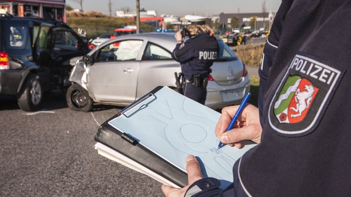 En Polizist hat auf einer Autobahn stehend eine Skizze des Unfallhergangs gezeichnet. Wir sehnen die Skizze in seiner Hand 