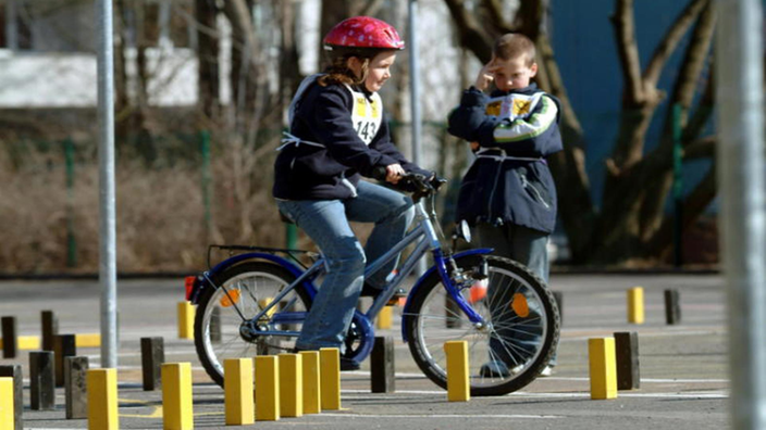 Ein Kind fährt auf einem Fahrrad durch einen Parcours. Ein anderes Kind schaut ihm dabei zu.