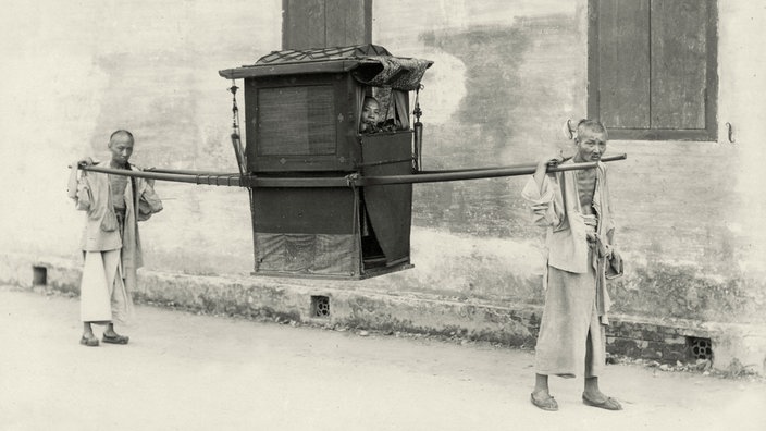 Schwarzweiß-Bild um 1880: Zwei Chinesen tragen eine Sänfte | Bildquelle: AKG Schwarzweiß-Bild um 1880: Zwei Chinesen tragen eine Sänfte