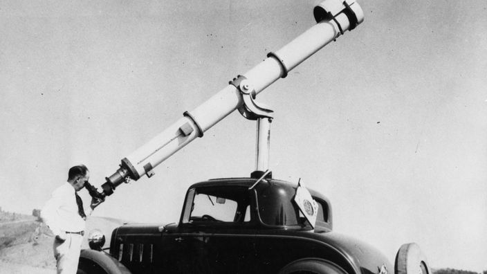 Ein Mann schaut durch ein riesiges Teleskop, das er auf sein Autodach moniert hat.