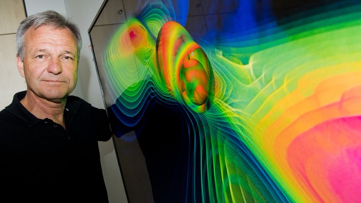 Karsten Danzmann vor einer Visualisierung von Gravitationswellen