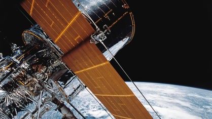 Das Foto zeigt Teile des riesigen Hubble-Weltraumteleskops. Im Hintergrund sind das All und die Erde zu sehen.