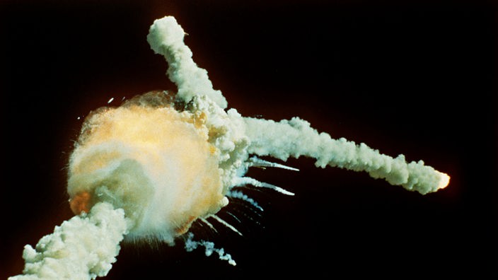 Die Challenger explodiert als Feuerball. Glühende Teile ziehen Rauchwolken hinterher.