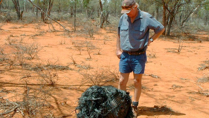 EinMann steht im australischen Busch neben einem Metallklumpen – wahrscheinlich ein Stück Weltraumschrott von einer Rakete