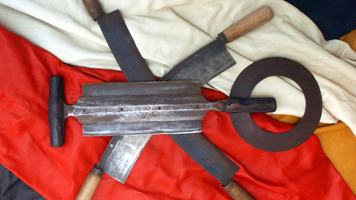 Drei traditionelle Gerberwerkzeuge, die gekreuzt auf farbigem Leder liegen.