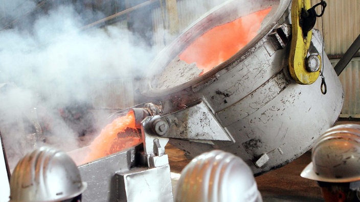 Mitarbeiter einer Aluminiumhütte befüllen einen Schmelzofen mit flüssigem Aluminiumoxid