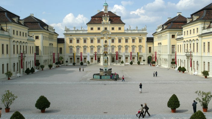 Die Front des Ludwigsburger Schlosses. Davor ein großer Platz, auf dem vereinzelt Menschen zu sehen sind.