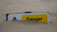 Schild mit der Aufschrift 'Danger' versinkt im Sand.
