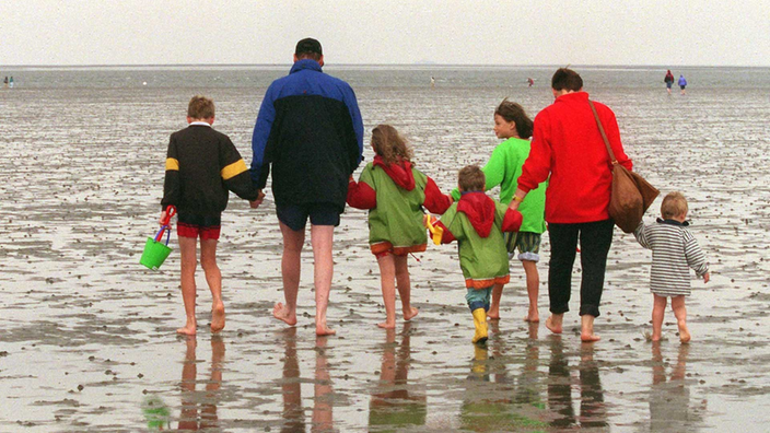 Diese Bild zeigt eine Familie bei ihrer Wanderung durch das Watt. Die Eltern halten die kleinsten Kinder an der Hand.