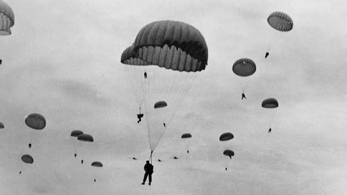 Das schwarz-weiße Foto zeigt ein Geschwader von Fallschirmjägern am Himmel.