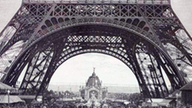 Der Holzstich zeigt den unteren Teil des Eiffelturms, unter dem mehrere Menschen herumwandern.