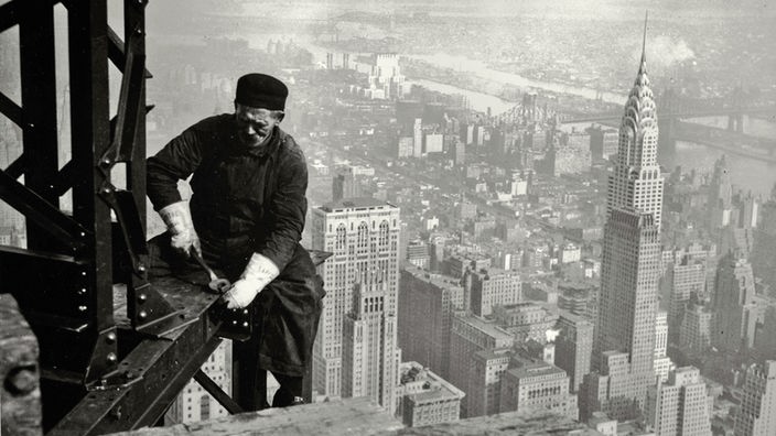 Ein Arbeiter beim Bau des Empire State Building 1930, im Hintergrund die Skyline von New York mit dem Chrysler Building.