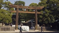 Shinto-Schrein mit zwei hölzernen Grundpfeilern und einem Querbalken. Darunter hindurch läuft eine Prozession von Mönchen.