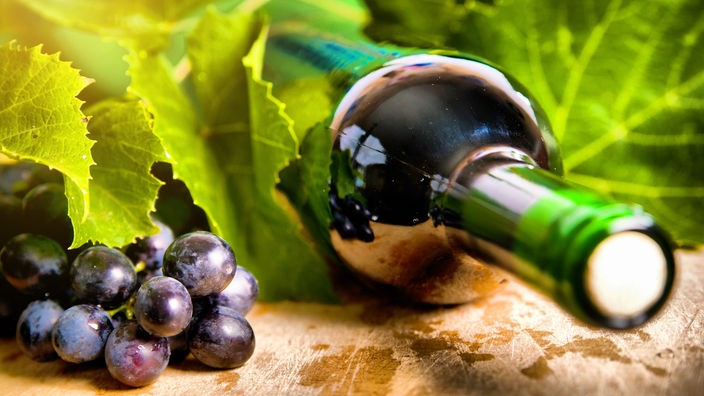 Eine Weinflasche liegt neben roten Weintrauben und Weinblättern.