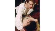 Romantischer Vampir in weißem Rüschenhemd nach Biss bei seinem liegenden Opfer. 