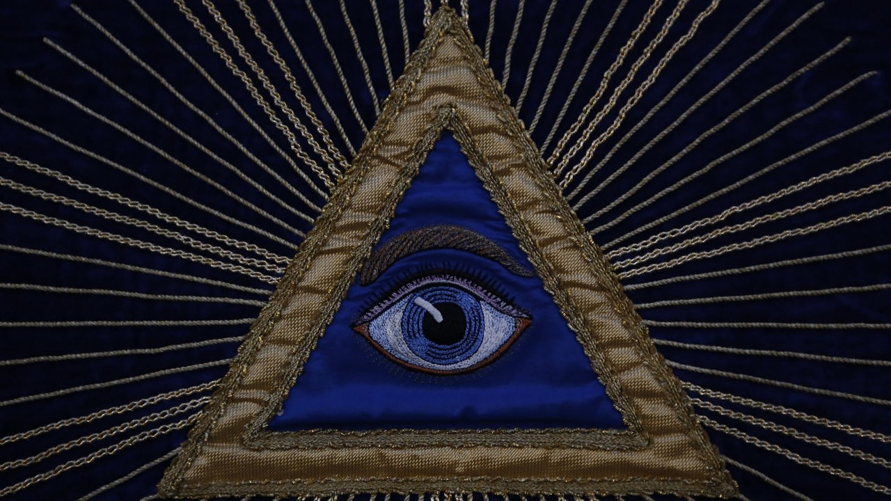 Stickerei auf der ein Auge abgebildet ist, eingerahmt von einem goldenen Dreieck