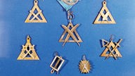 Eine Sammlung von Anhängern und Abzeichen der Freimaurer in Form von metallenen Dreiecken und Winkeln.