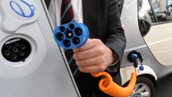 Mann hält Stecker von Elektroauto, Auto im Hintergrund.