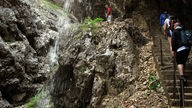 Eine Gruppe Wanderer sind in der Höllentalklamm von steilen Felsen umgeben